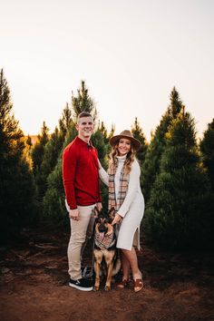 a man and woman standing next to a dog on a dirt road with trees in the background