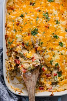 a casserole dish filled with chicken, cheese and veggies on a wooden spoon