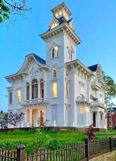 a large white house sitting on top of a lush green field next to a fence