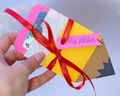 a hand holding an envelope with a red ribbon and name tag attached to the front