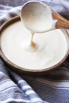 a spoon full of yogurt sitting on top of a wooden bowl next to a blue and white towel