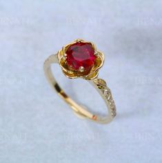 a gold ring with a red stone in the center and two white diamonds around it