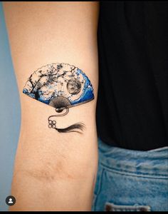 a woman's arm with a tattoo on it that has an image of a rock and a fan