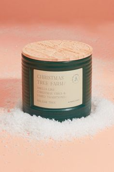 a candle is sitting in the snow on top of some white flakes and it has a label that says christmas tree farm