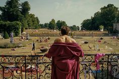 a woman in a red dress is looking over a fence at an open area with many people