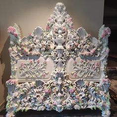 an intricately decorated white and pink headboard with flowers on the sides, in front of a wall