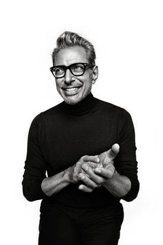 a black and white photo of a man with glasses smiling at the camera while holding his hands together