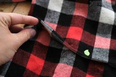 someone is stitching a green patch on a red and black flannel shirt