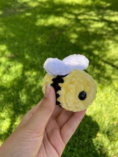 a hand holding a small yellow and black stuffed animal with a white top on it's head