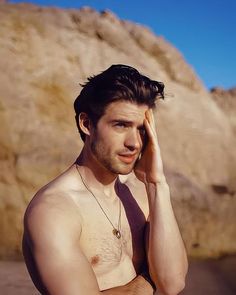 a shirtless man holding his hand to his head while standing in front of a mountain