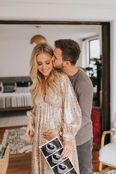 a pregnant couple kissing in their living room while holding a photo frame with the baby's first year printed on it