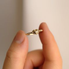 a hand holding a tiny gold ring with a skull on it's side,