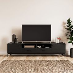 a flat screen tv sitting on top of a black entertainment center next to a potted plant