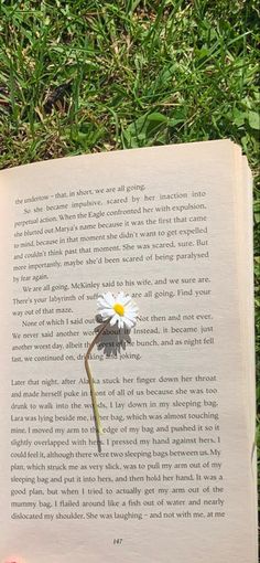 an open book laying in the grass with a flower sticking out of it's middle