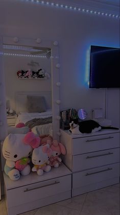 a bedroom with white furniture and hello kitty stuffed animals on top of the dressers