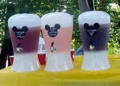 three glasses with mickey mouse ears on them sitting on top of a table in front of trees