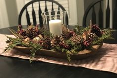 a candle is lit on a wooden tray with pine cones and berries