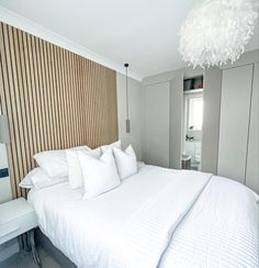 a white bed sitting in a bedroom next to a tall wooden headboard with pillows on it