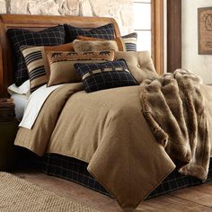 a bed covered in brown and black comforter next to a stone wall with windows