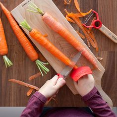 a person cutting carrots with a knife on a cutting board next to other vegetables