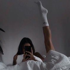 a woman laying in bed with her legs up and holding a cell phone to her ear