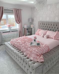 a large bed with pink sheets and pillows in a room next to a chandelier