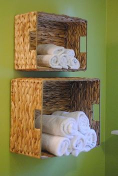 two baskets with towels hanging on the side of them in front of a green wall