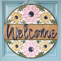 a welcome sign hanging on a blue door with flowers and leaves painted on the front