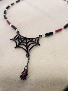 Just in time for Halloween, this spider web necklace is sure to delight. Fully hand made links make this a one-of-a-kind piece. The links feature black and red glass beads. This necklace measures 16.5 inches in total length. The handmade links are crafted from silver filled wire. The closure is a sterling silver lobster claw clasp. It is a very lightweight piece, made from tarnish resistant silver wire, so it is comfortable for all day wear and will last for years to come. And to top it all off, the web is complete with a hanging spider sporting a pink jewel. Gothic Black Necklace With Lobster Clasp, Black Halloween Necklace With Lobster Clasp, Black Gothic Necklace With Lobster Clasp, Adjustable Black Vampire Necklace, Adjustable Black Vampire Style Necklaces, Handmade Black Vampire Necklace, Adjustable Red Necklace For Halloween, Handmade Black Witchy Necklace, Handmade Red Necklaces For Halloween