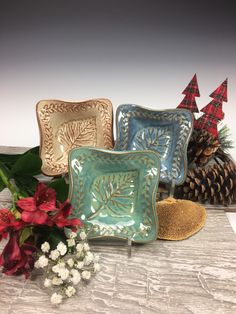 three decorative plates sitting on top of a table next to some flowers and pine cones