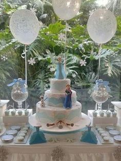 a table topped with a cake covered in frosting next to lots of balloons and snowflakes