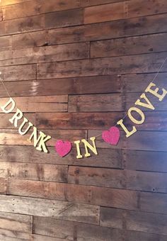 a sign that says drunk in love on a wooden wall with hearts hanging from it