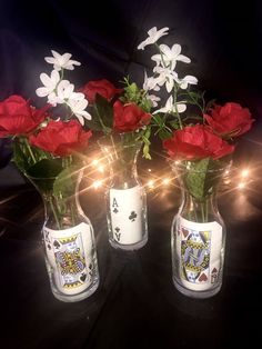 three vases filled with red and white flowers on top of a black table covered in lights