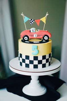 a birthday cake decorated with a race car and bunting on the top is ready to be eaten