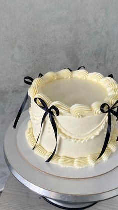 a white cake with black ribbon and bow on top sitting on a silver platter