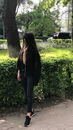 a woman with long hair walking down the sidewalk talking on her cell phone while wearing black sneakers