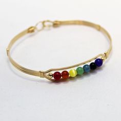 "A contemporary little bracelet of five strands of 14kt gold filled wire with a center design featuring the seven colors of the chakra in 4mm beads, accented with two smaller gold beads. Perfect for the girl who loves to get her \"metaphysical\" on! Stackable, too, along with many of my other wirewrapped bracelets! The sturdy built-in hook and eye clasp is easy to get on and off by yourself. Choose the size you need for a comfortable custom fit." Adjustable Flexible Yellow Gold Bracelets, Elegant Adjustable Rainbow Beaded Bracelets, Gold Nickel-free Bracelets For Friendship, Adjustable Yellow Gold Flexible Bracelets, Adjustable Yellow Gold Nickel-free Bracelet, Nickel-free Gold Bracelet For Friendship, Gold Nickel-free Bracelet For Friendship, Adjustable Spiritual Bracelet In 14k Gold Filled, Adjustable 14k Gold Filled Spiritual Bracelet