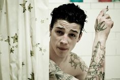 a man with tattoos on his arms and arm is looking at the camera in front of a shower curtain