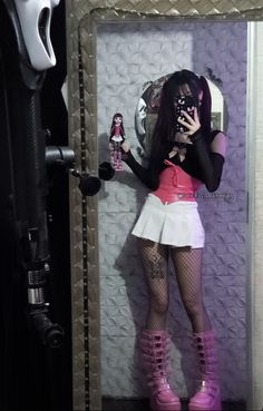 a woman dressed in pink and white holding a cell phone while standing next to a mirror