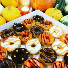 a box filled with lots of different flavored donuts next to pumpkins and gourds