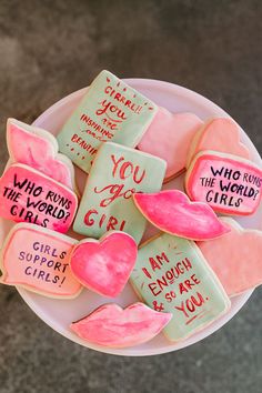 pink and green conversation cookies with writing on them in a white bowl sitting on the ground