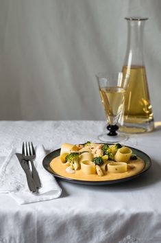 a plate with pasta and broccoli on it next to a glass of wine