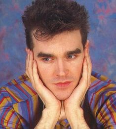 a young man with his hands on his face posing for a photo in front of a blue background