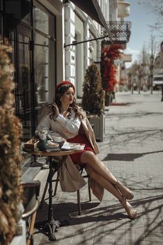 a woman sitting at a table on the side walk talking on her cell phone and eating