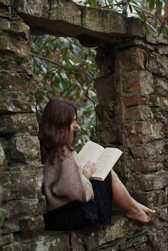 a woman sitting on a stone wall reading a book