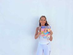 a woman is holding up a magazine in front of her face while standing against a white wall