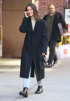 a woman talking on her cell phone while walking down the street with another man in the background