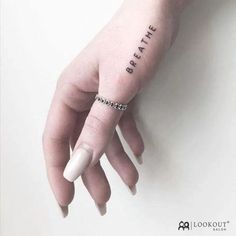 a woman's hand with a small tattoo saying breathe on the left side of her finger