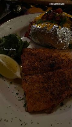 a white plate topped with fish next to a salad and baked potato covered in foil