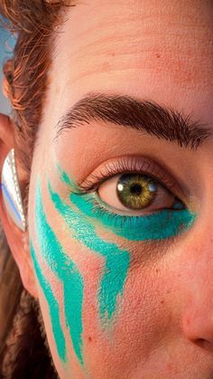 a woman with blue paint on her face and green eyeliner is looking at the camera